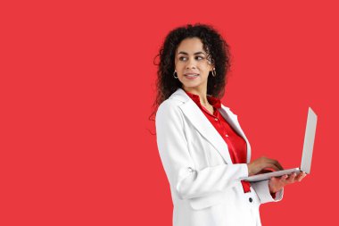 Young African-American businesswoman using laptop on red background