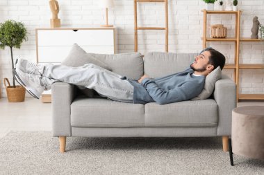 Handsome young man lying on sofa in living room