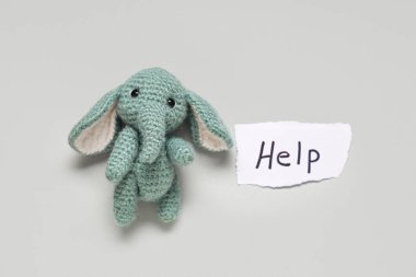 Paper piece with word HELP and toy elephant on light background. Domestic violence concept