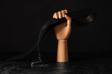 Wooden hand with belt on dark background. Domestic violence concept