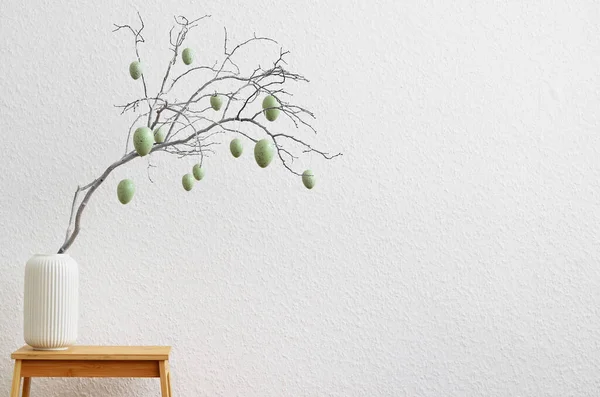 Vase with tree branch and Easter eggs on step ladder near light wall