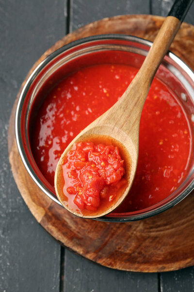 Кастрюля и ложка с вкусным томатным соусом на темном деревянном фоне