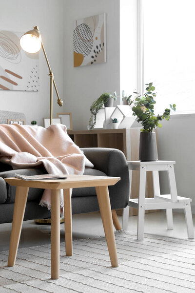 Interior of light living room with glowing lamp, table and sofa