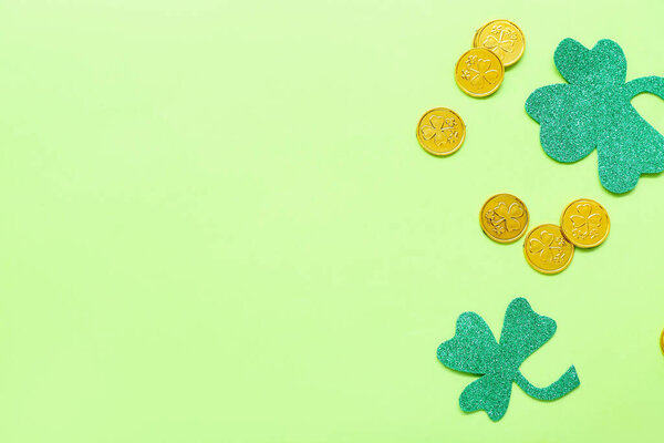 Golden coins with paper clovers on light green background. St. Patrick's Day celebration