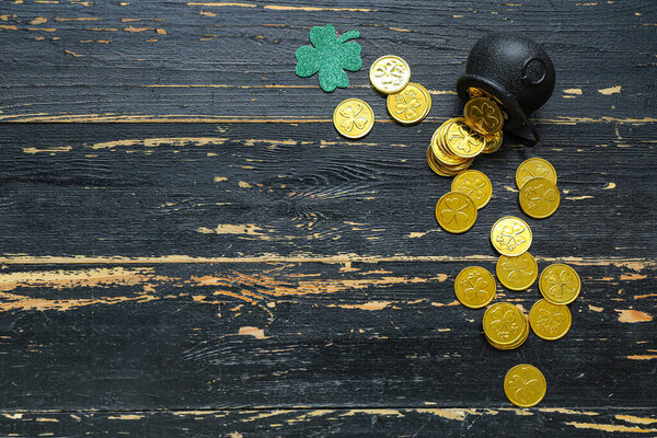 Pot with golden coins and paper clover on black wooden background. St. Patrick's Day celebration