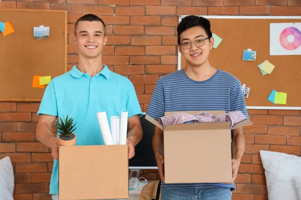 Male students with boxes in dorm room on moving day