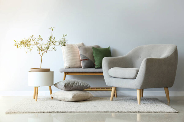 Grey armchair and bench with soft cushions near white wall