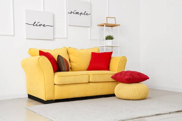 Yellow sofa with cushions and pouf near white wall