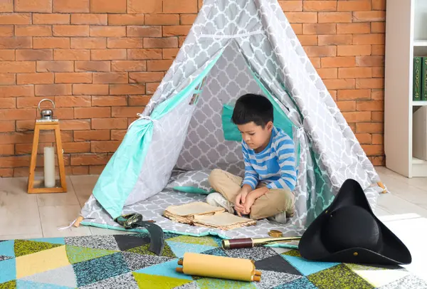 Cute little boy with adventure book in play tent at home