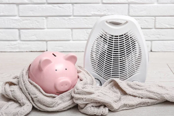Electric fan heater, piggy bank and scarf on floor. Heating season