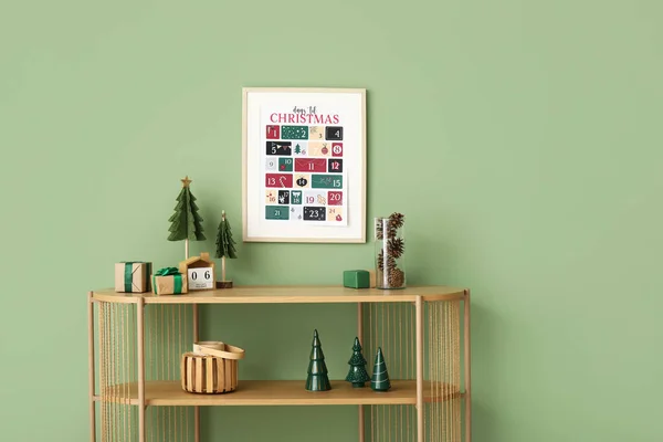 Shelf unit with presents, decor and Christmas calendar on green wall
