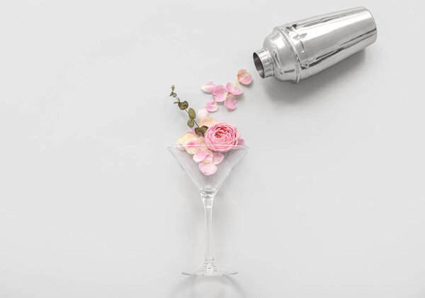 Composition with glass, beautiful flowers and cocktail shaker on light background