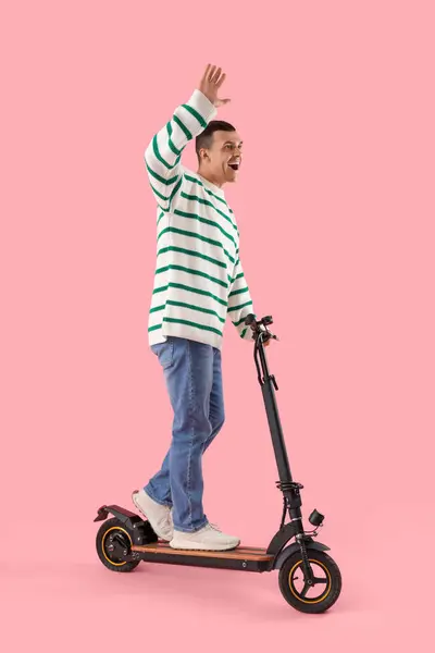 Young man with kick scooter on pink background