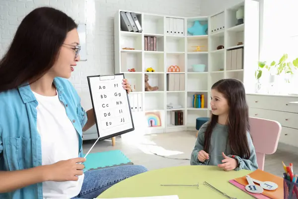 Little girl and speech therapist showing clipboard with letters in office