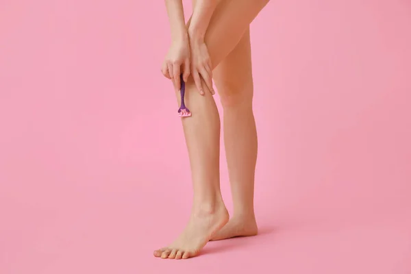 Beautiful young woman with razor shaving legs on pink background, closeup