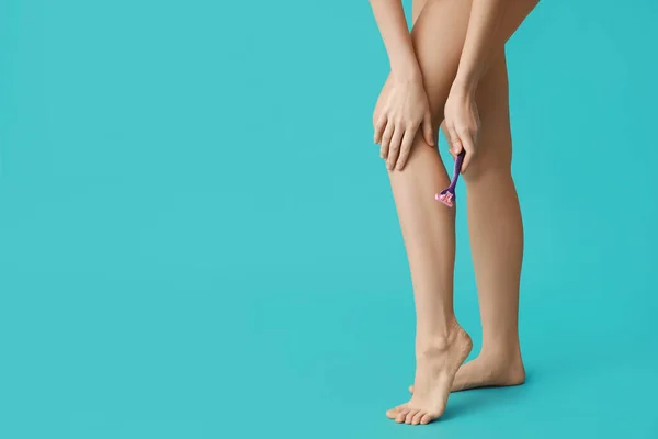 Beautiful young woman with razor shaving legs on turquoise background, closeup