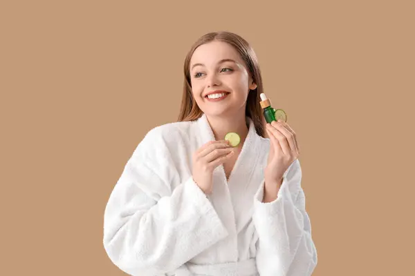 Young Woman Bathrobe Cucumber Slices Serum Beige Background — стоковое фото