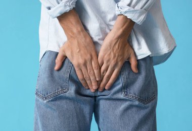 Young man with hemorrhoids on blue background, back view