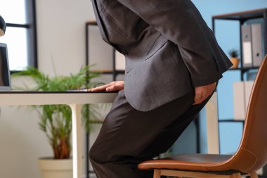 Young businessman with hemorrhoids sitting on chair in office