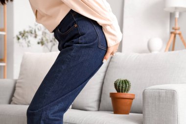Young woman with hemorrhoids and cactus on sofa at home, closeup