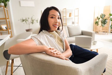 Young Asian woman sitting in armchair at home