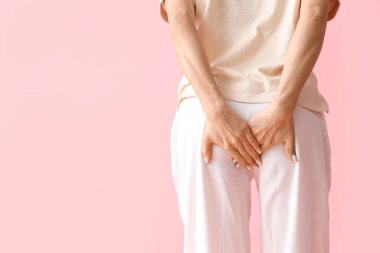 Young woman with hemorrhoids on pink background, back view