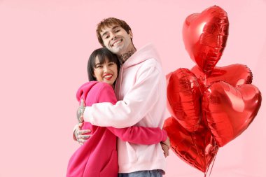Young couple with balloons hugging on pink background. Valentine's Day celebration