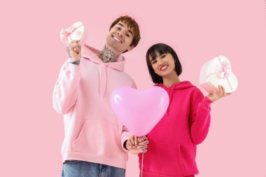 Young couple with gift boxes and balloon on pink background. Valentine's Day celebration