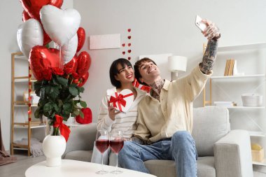 Young couple with gift taking selfie at home on Valentine's Day