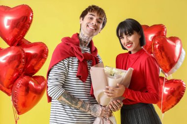 Young couple with roses and balloons on yellow background. Valentine's Day celebration