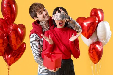 Young man greeting his beloved with gift on yellow background. Valentine's Day celebration