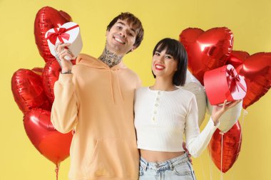Young couple with gift boxes and balloons on yellow background. Valentine's Day celebration