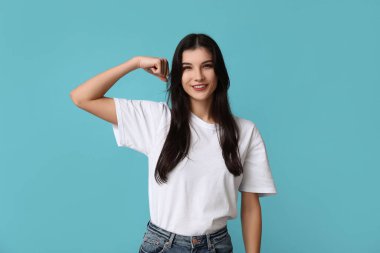 Young woman flexing muscles on blue background. Feminism concept