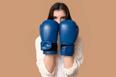 Young woman in boxing gloves on beige background. Feminism concept