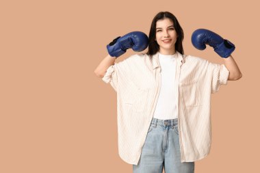 Young woman in boxing gloves celebrating success on beige background. Feminism concept