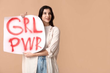 Young woman with sign GRL PWR on beige background. Feminism concept