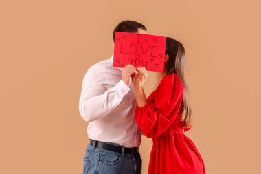 Lovely couple holding greeting card with text I LOVE YOU on beige background. Valentine's Day celebration