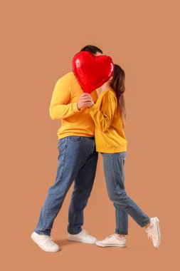 Lovely couple covering faces with heart-shaped balloon on beige background. Valentine's Day celebration