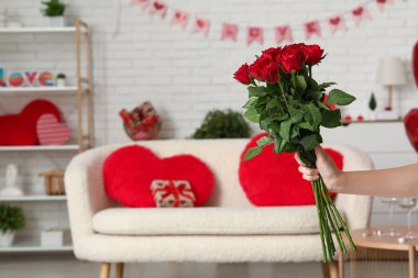 Female hand holding bouquet of red roses in living room, closeup. Valentine's Day celebration