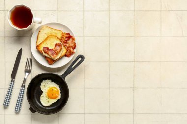Composition with toasts, tasty bacon, fried egg and cup of tea on light tile background