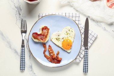 Plate with hearts made of tasty fried egg, bacon and cutlery on light background