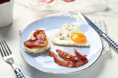 Plate with tasty bacon, hearts made of fried egg and bread on light background, closeup