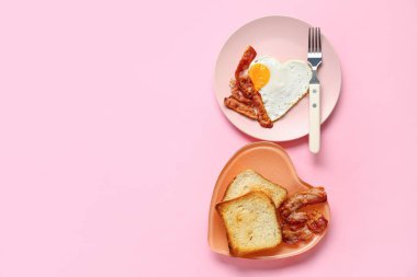 Plates with tasty bacon, heart made of fried egg and toasts on pink background