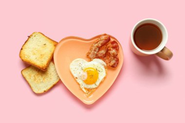 Plate with fried egg, tasty bacon, toasts and cup of tea on pink background