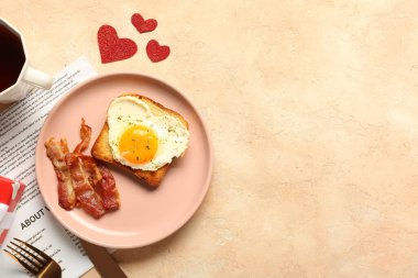 Composition with tasty bacon, fried egg, toast, cup of tea and newspaper on beige background