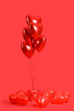Heart-shaped balloons and gift box on red background. Valentine's Day celebration