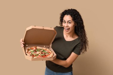 Beautiful young happy African-American woman with delicious pizza on beige background