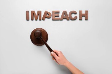Female hand with judge gavel and word IMPEACH on white background