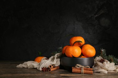 Bowl with tasty tangerines and cinnamon on wooden table