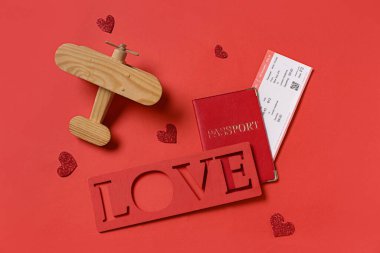 Word LOVE with passport, ticket, wooden airplane and hearts on red background. Valentine's Day celebration